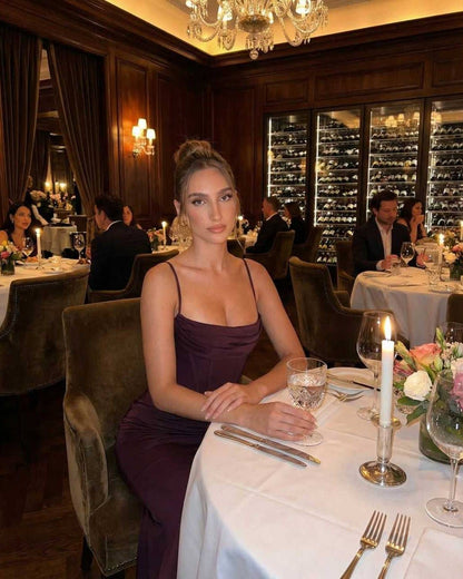 Celeste Maxi Dress worn at a refined dinner setting, featuring sleek sheath silhouette with spaghetti straps in deep plum color.