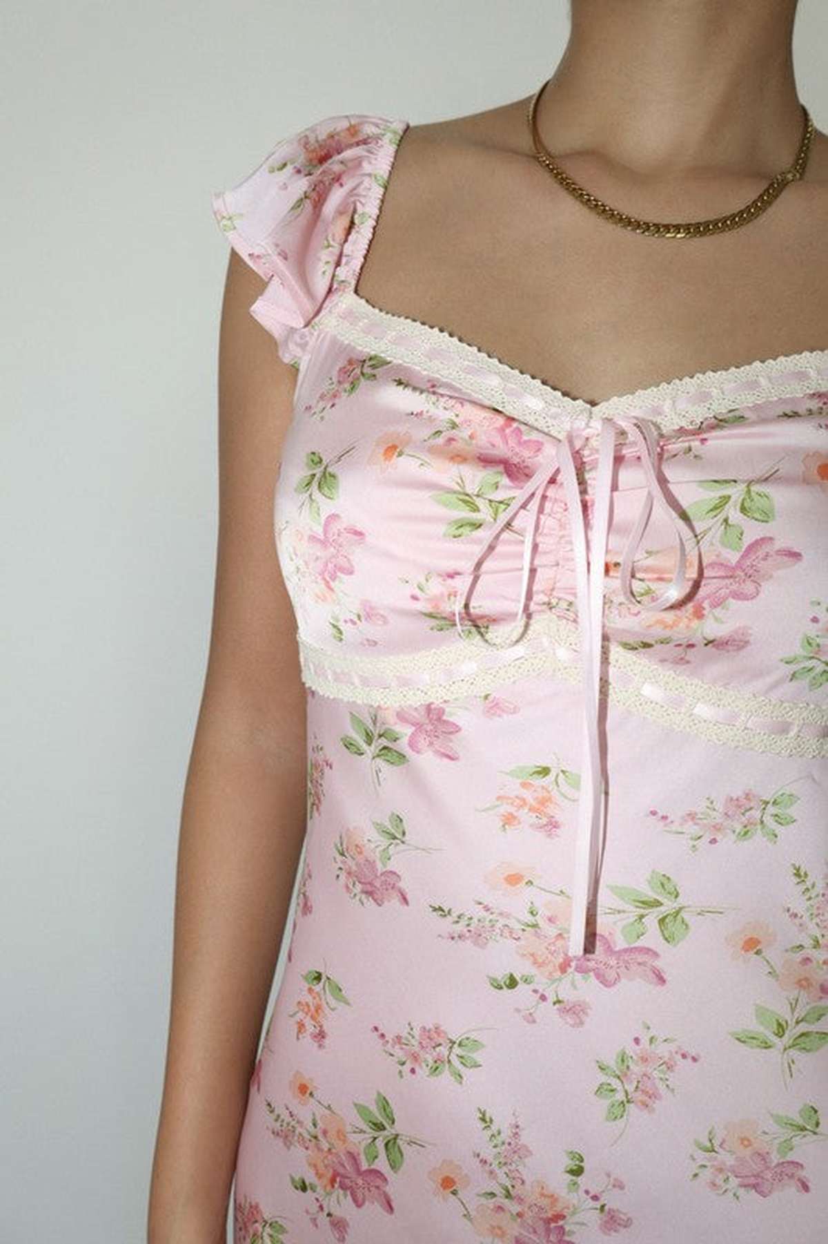 Close-up of Celeste Women's Dress featuring pink floral patterns, flutter sleeves, and delicate lace trim, perfect for summer or weddings.