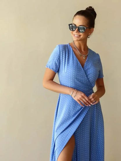 Celeste Wrap Maxi Dress in soft blue polka dot fabric with V-neckline and thigh-high slit, styled with sunglasses.