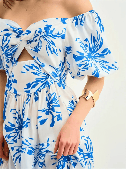 Close-up of woman in white maxi dress with cornflower blue floral print and puff sleeves, featuring a knotted sweetheart neckline.