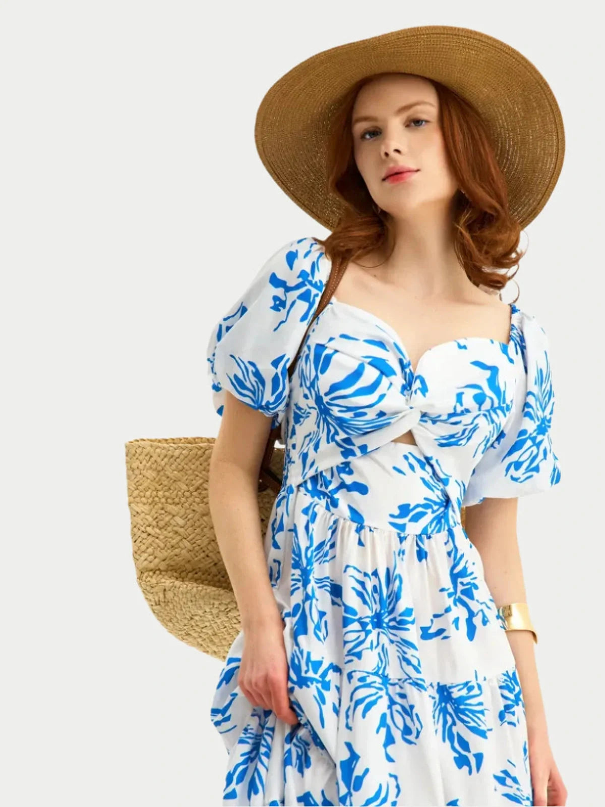 Woman in white maxi dress with cornflower blue floral print, sweetheart neckline, and puff sleeves, wearing a straw hat.
