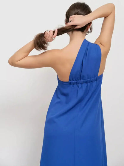 Back view of a woman styling her hair while wearing a cerulean one-shoulder maxi dress.