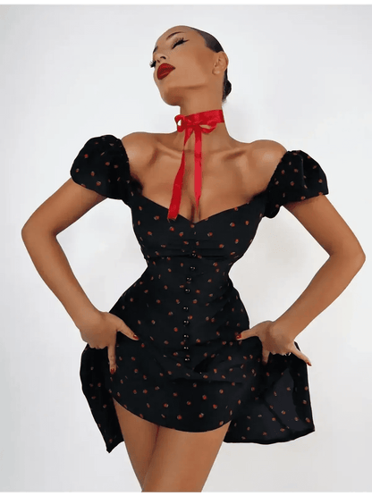 Woman modeling a Cherry Kiss Mini Dress featuring cherry print, puff sleeves, and a sweetheart neckline.
