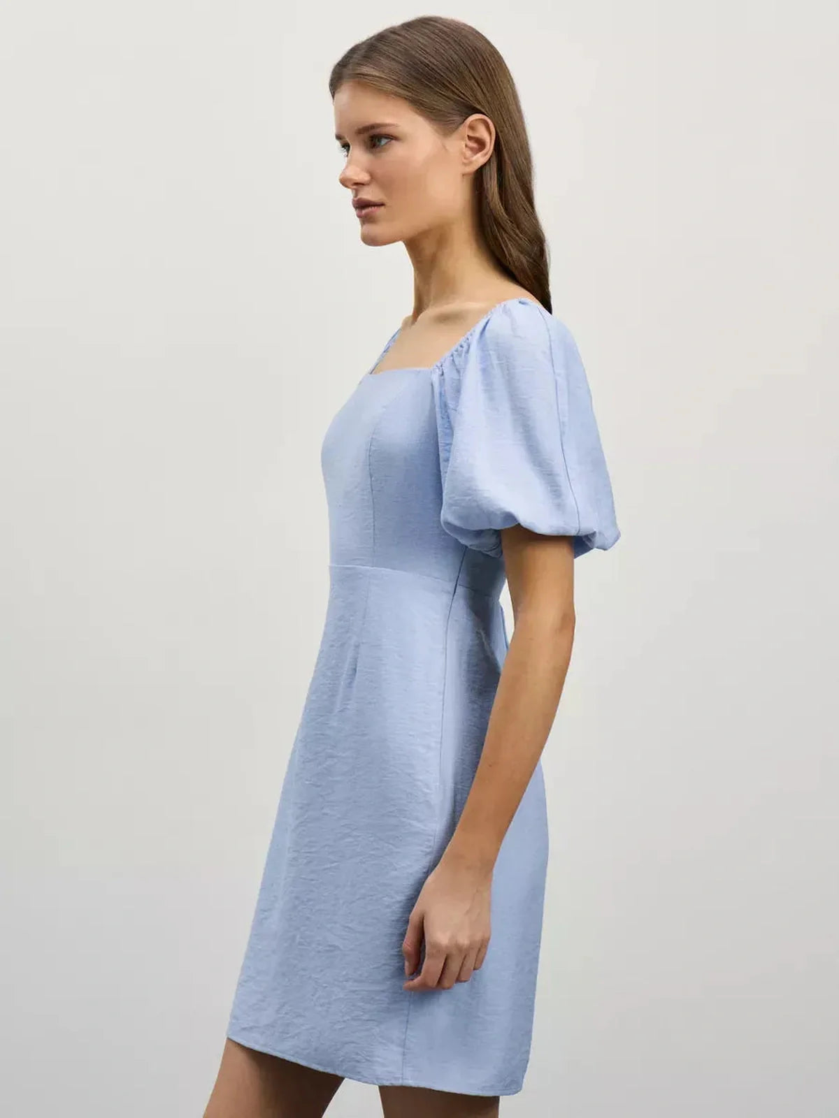 Side view of a woman wearing the Cloudline Mini dress in light blue with puff sleeves and a square neckline.