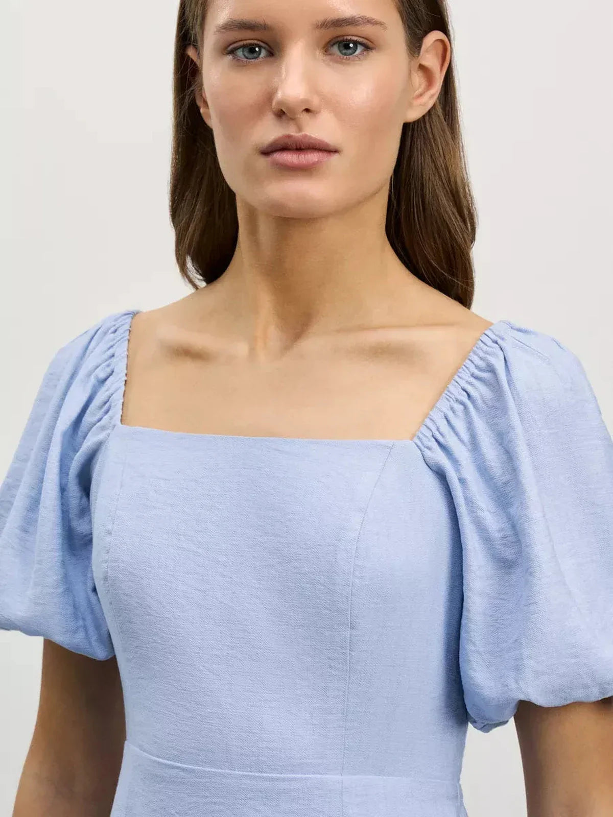 Close-up of a model wearing the Cloudline Mini dress in light blue featuring a square neckline and puff sleeves.