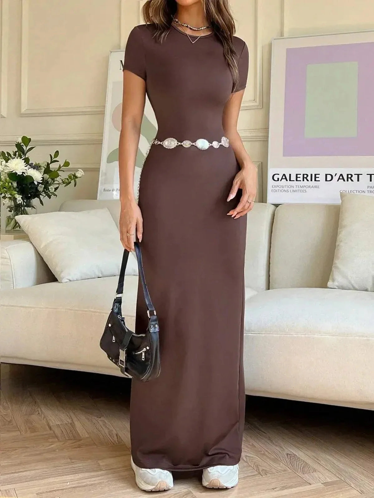 Cocoa Curve Maxi Dress featuring sleek fit, back slit, and asymmetric neckline, styled casually in a modern living space.