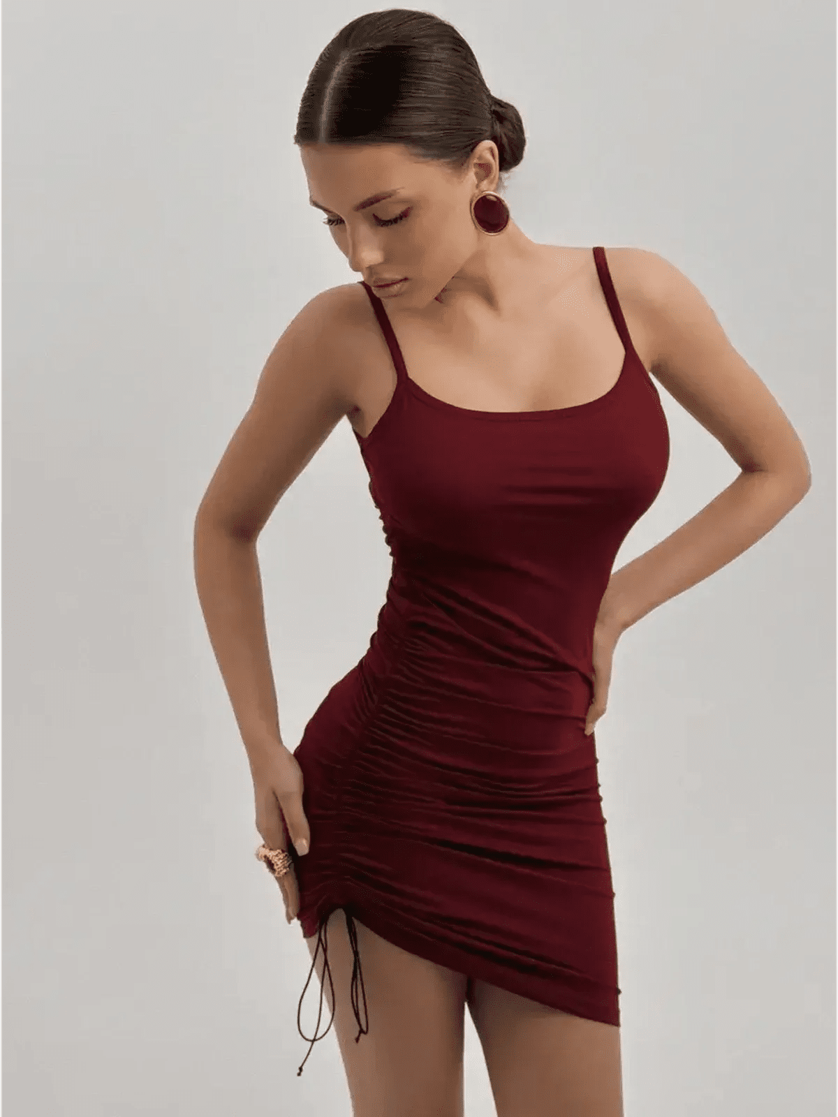 Model in a fitted crimson mini dress with spaghetti straps and side ruching, perfect for summer and special occasions.