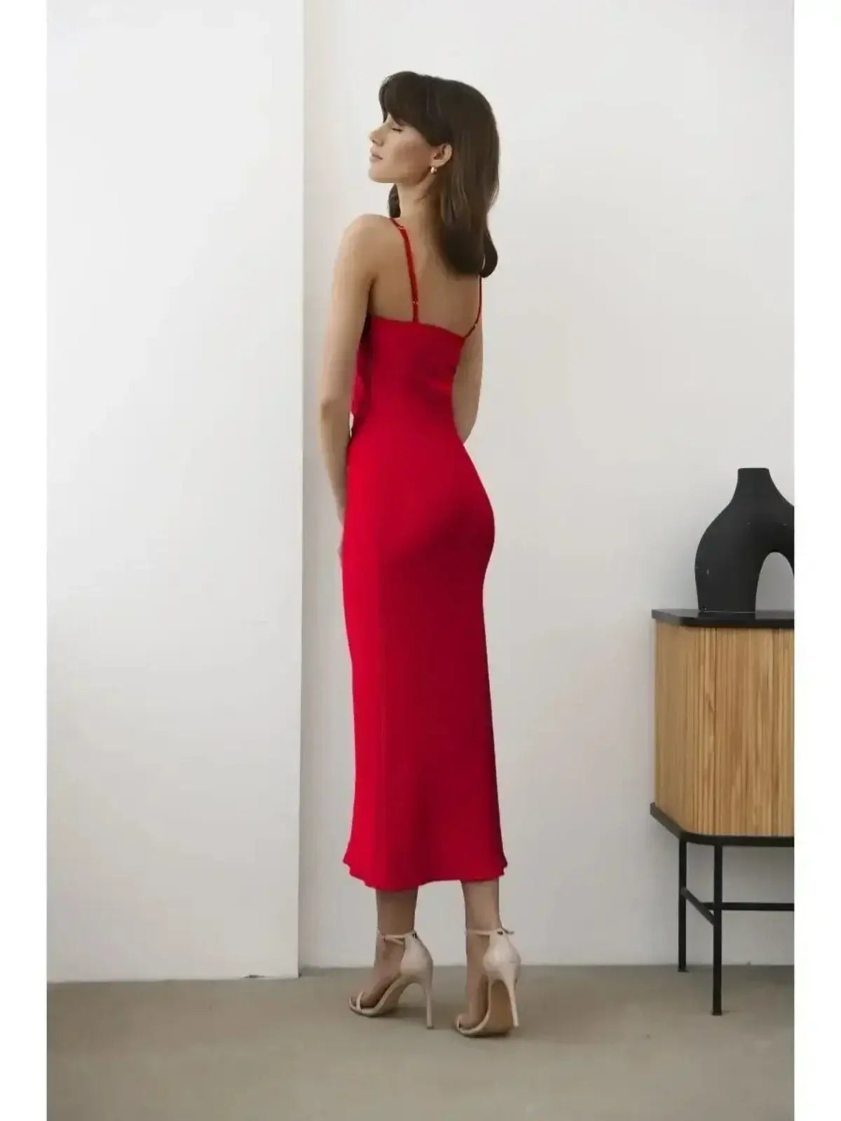 Back view of a model in a sleek red satin midi dress, showcasing sultry elegance and a figure-flattering silhouette.