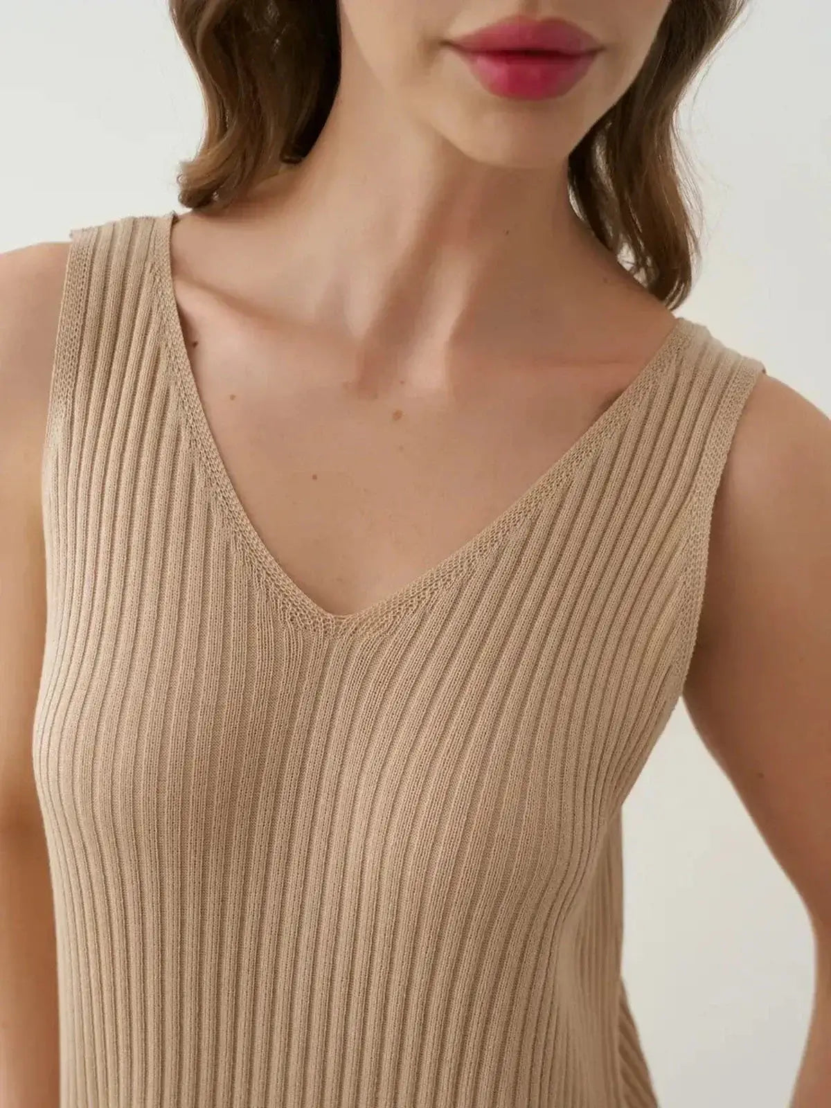 Close-up of a woman wearing a beige ribbed knit sleeveless top featuring a V-neckline.