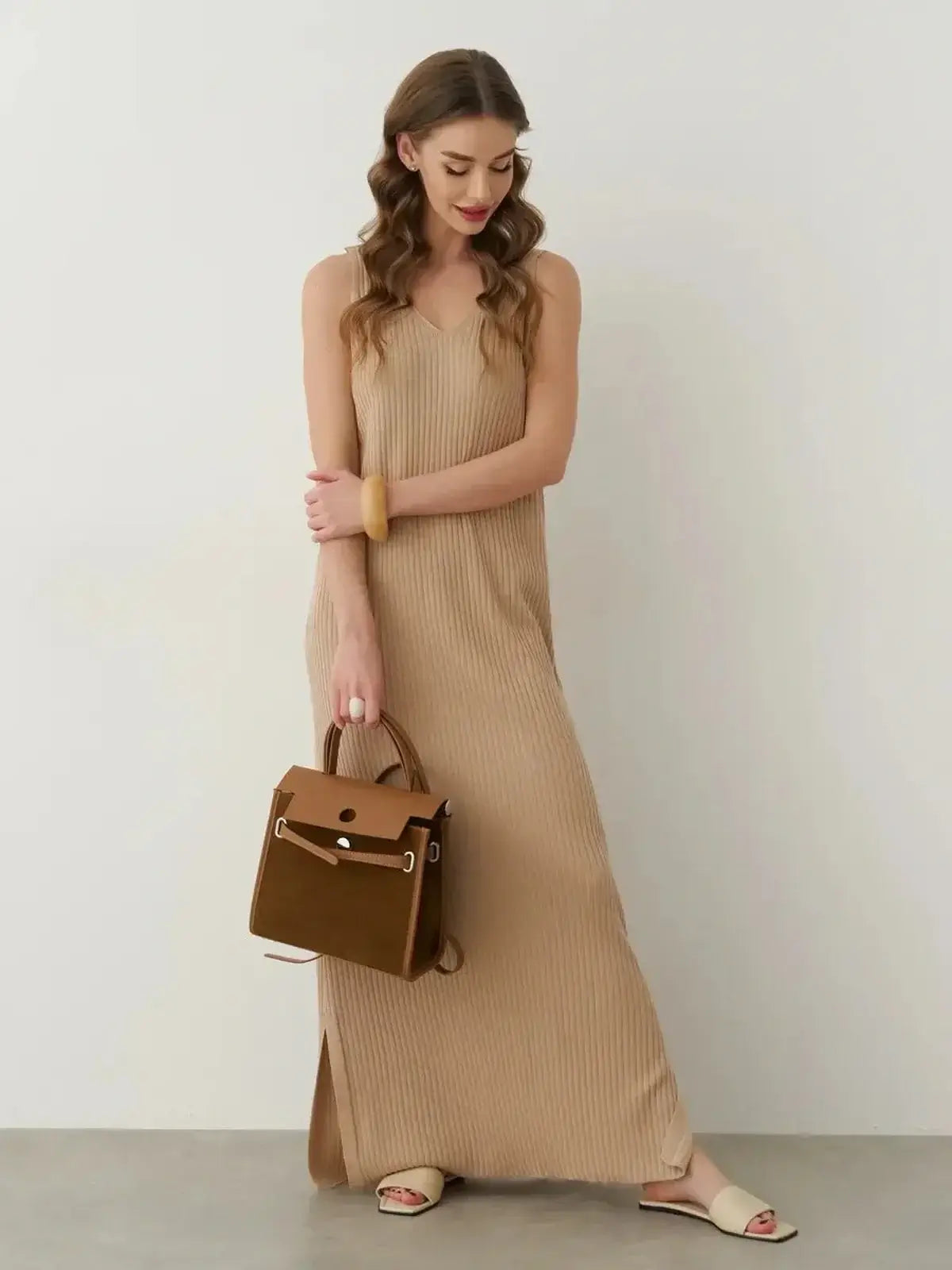 Model wearing a neutral ribbed maxi dress with a side slit, holding a brown handbag, showcasing summer elegance.