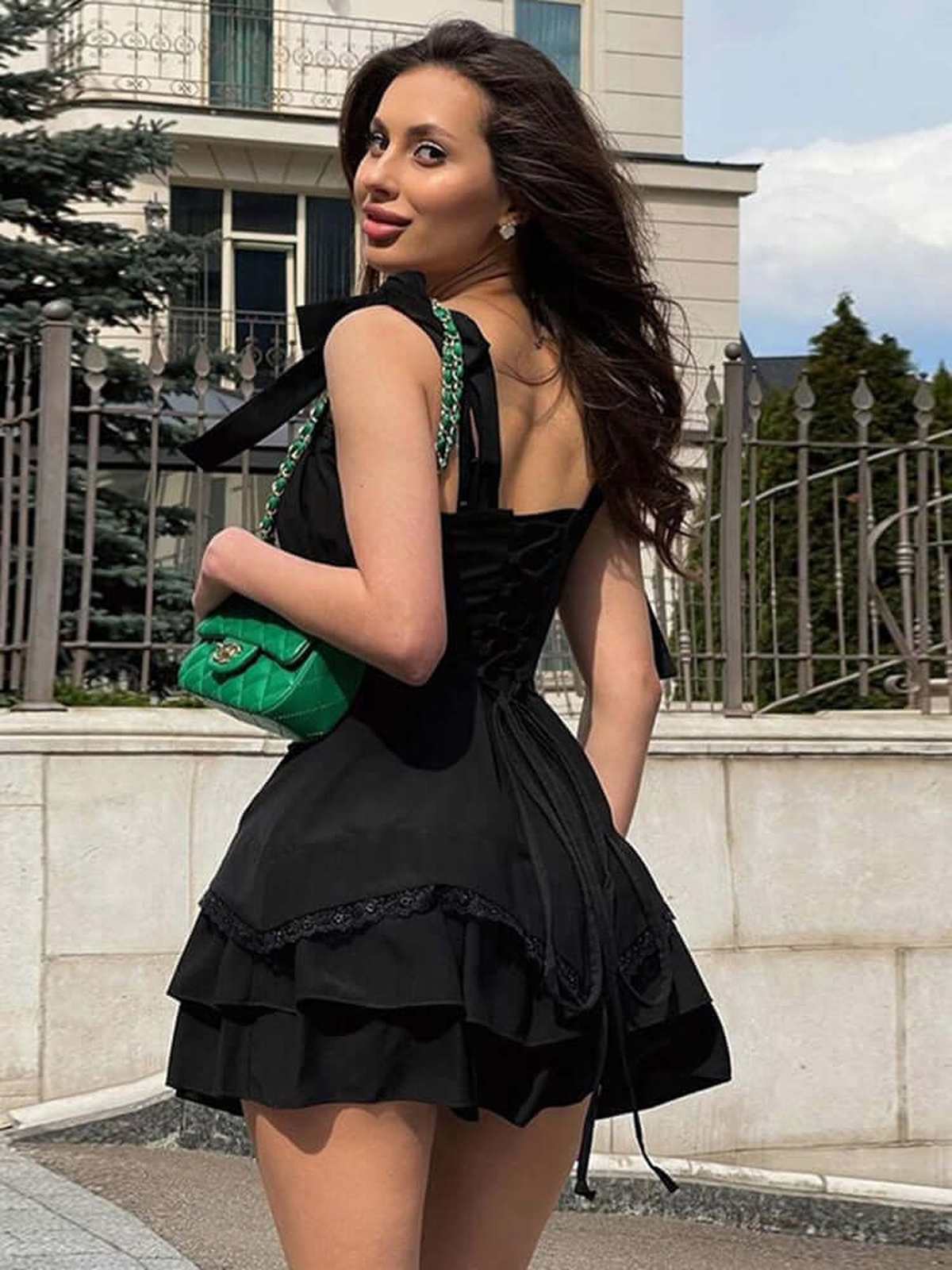 Woman in a black mini dress with ruffles, accessorized with a green handbag, showcasing summer fashion style.