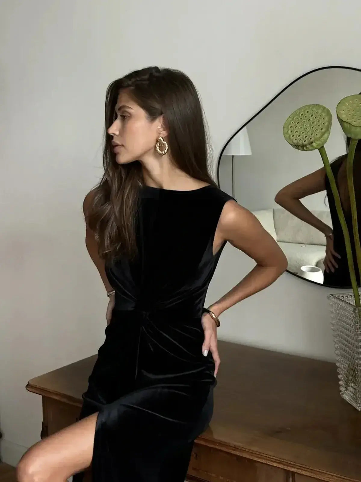 Woman modeling a black velvet Eclipse Maxi Dress with draped knot detail and thigh-high slit, exuding elegance.
