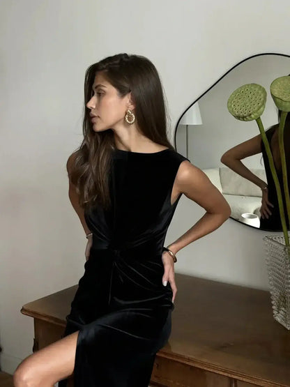 Woman modeling a black velvet Eclipse Maxi Dress with draped knot detail and thigh-high slit, exuding elegance.