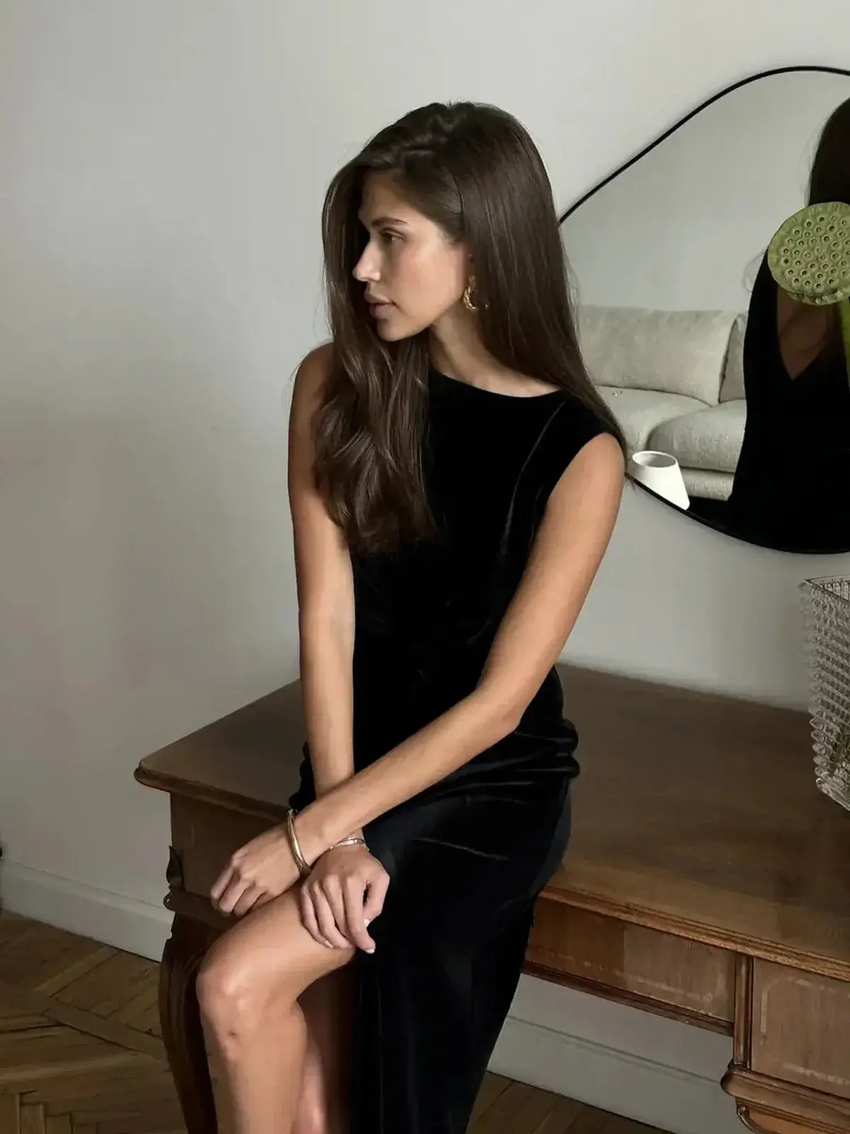 Model showcasing the Eclipse Maxi Dress in black velvet, featuring a sculpted bodice and sitting elegantly at a wooden table.