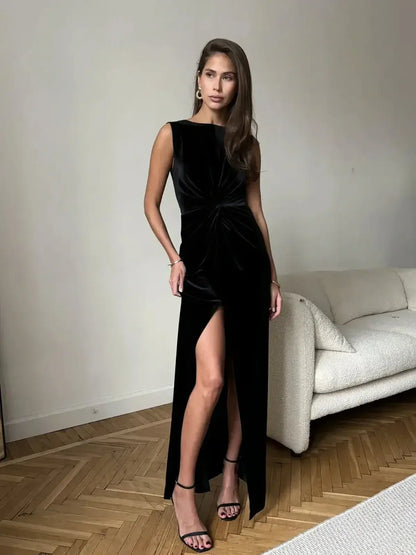 Model wearing the Eclipse Maxi Dress, a black velvet evening dress with a draped knot and thigh-high slit.