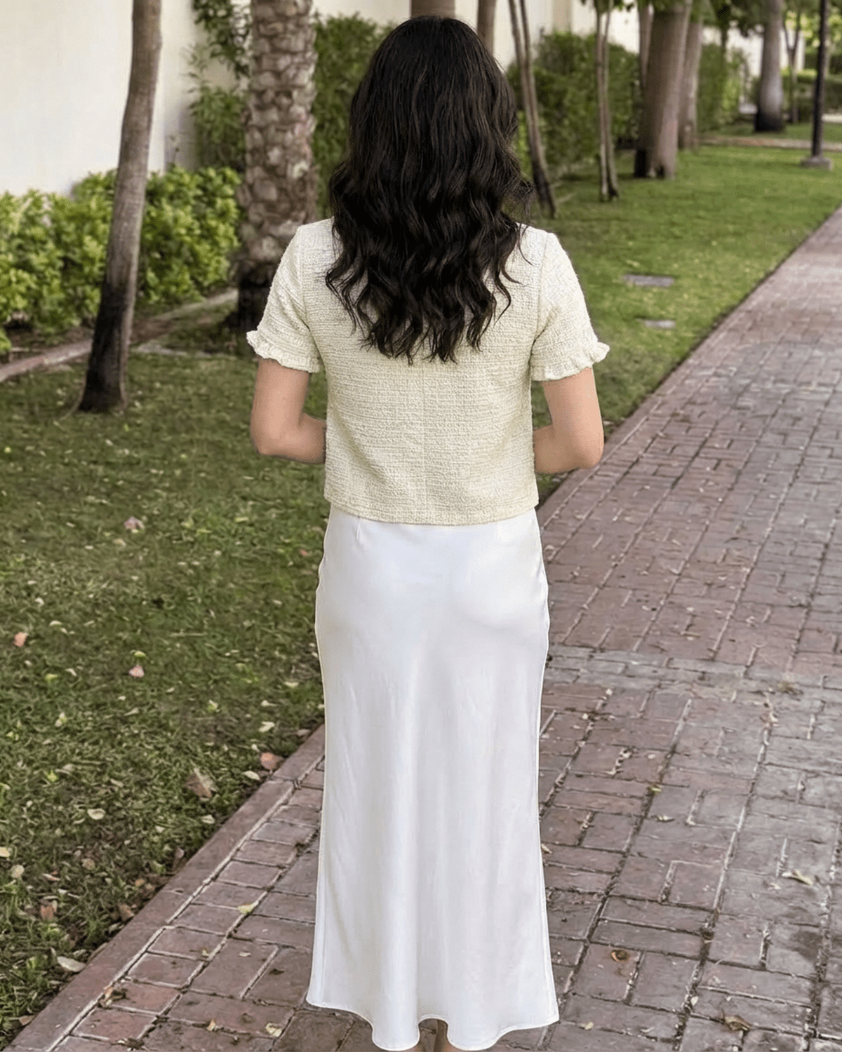 Back view of woman in Elara Cardigan, short sleeve knitwear by Lauven, paired with a flowing white skirt.