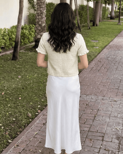 Back view of woman in Elara Cardigan, short sleeve knitwear by Lauven, paired with a flowing white skirt.
