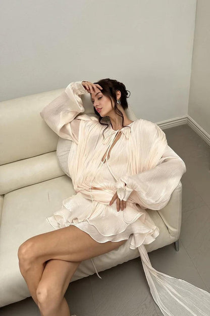 Model relaxing in a chic rose mini dress with pleated chiffon design, exuding elegance and femininity on a sofa.