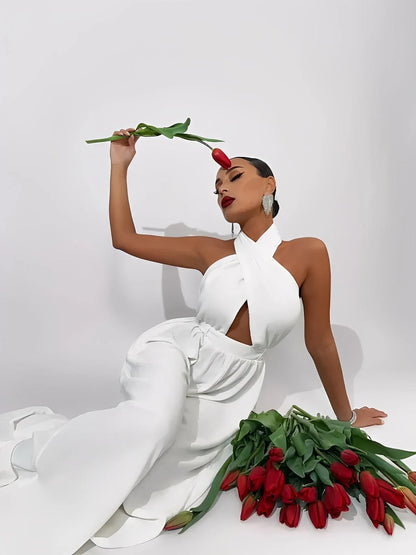 Model in an elegant Elysian jumpsuit holding a red tulip, surrounded by fresh tulips on a white background.