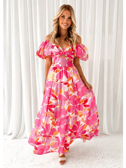 Model wearing the vibrant Flora Muse Maxi Dress featuring off-shoulder sleeves and floral prints in pink and orange.
