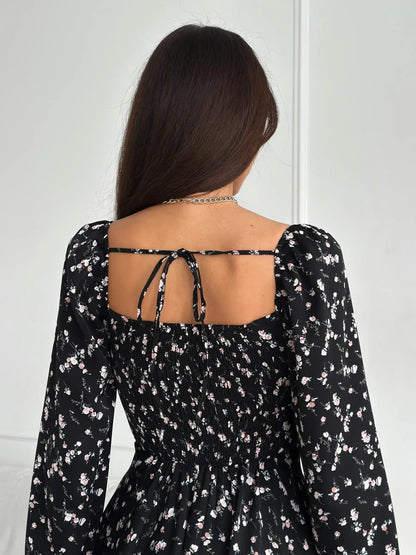Back view of a woman in a floral black mini dress with long sleeves, showcasing its stylish design.
