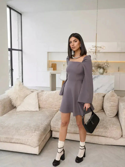 Model wearing a Graphite Bloom mini dress with flare sleeves in a modern living room setting.