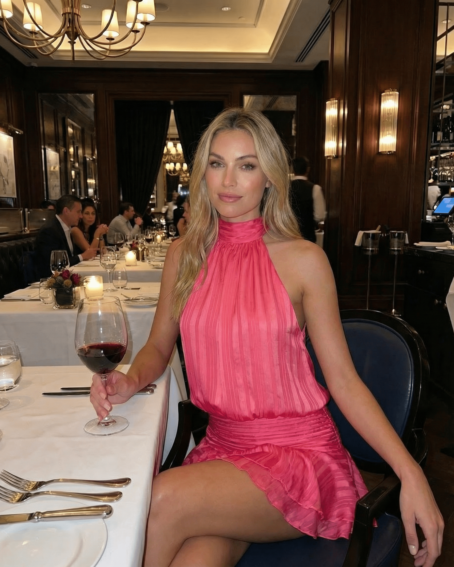 Woman enjoying dinner in a restaurant wearing the Roselle Mini Dress by Lauven, featuring a pleated design and halter neckline.