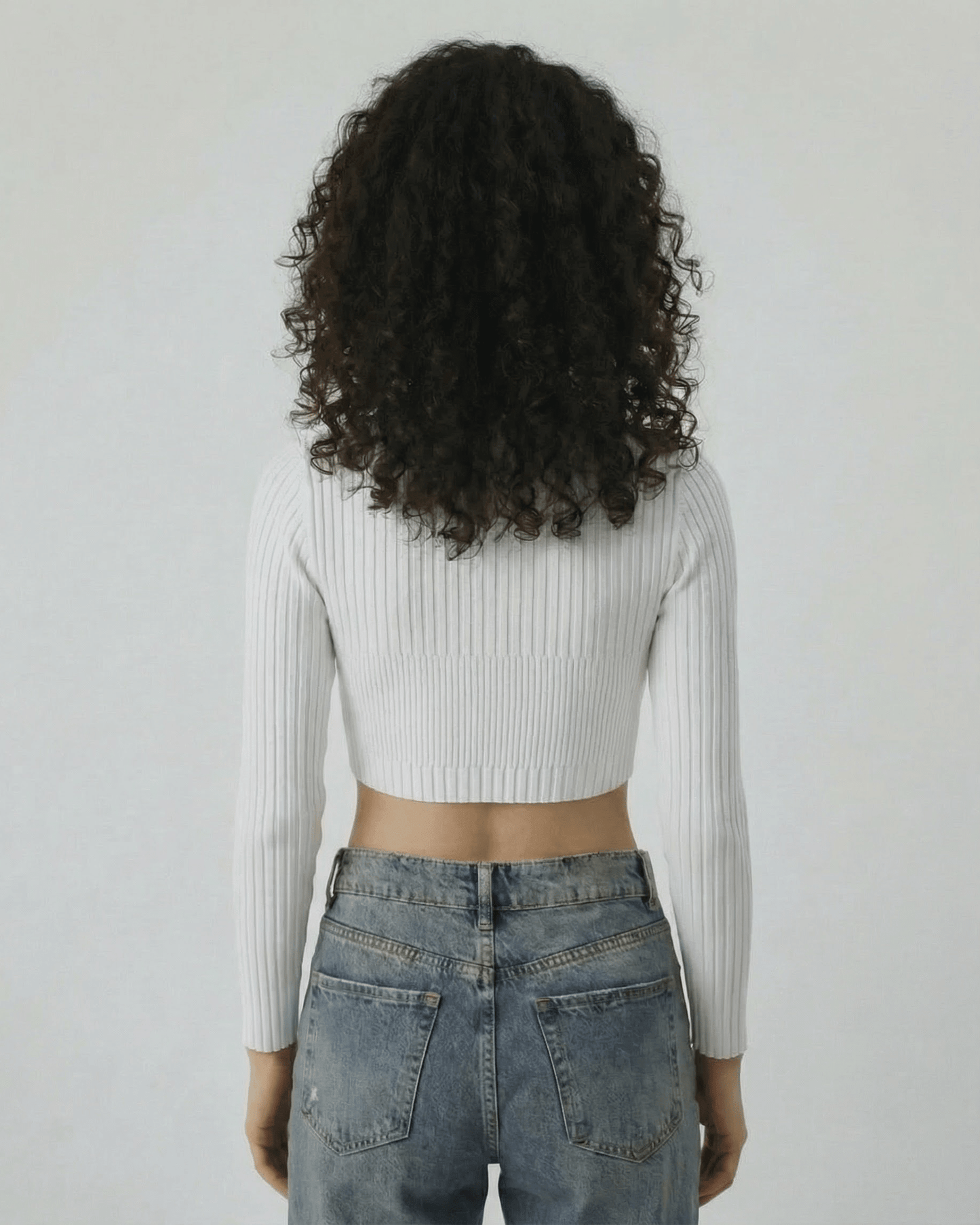 Back view of a woman wearing the Lauven Monaco Top, a white ribbed knit long sleeve cut out top.