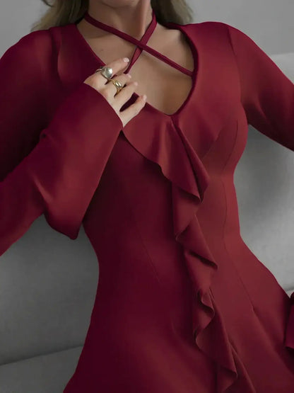 Close-up of a burgundy long sleeve mini dress featuring a V-neckline, cross-strap detailing, and ruffle accents.