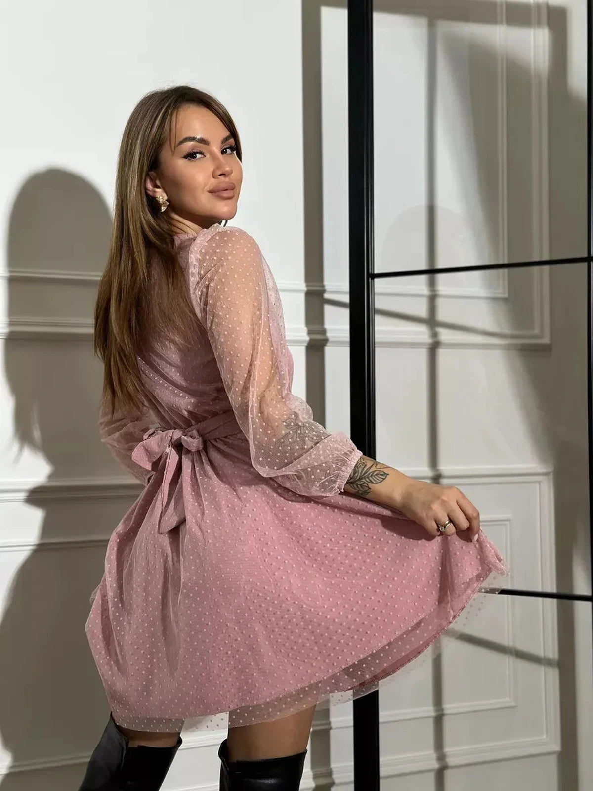 Woman modeling the Aurora Mini Dress by Lauven in elegant powder pink chiffon with sheer polka dot sleeves.