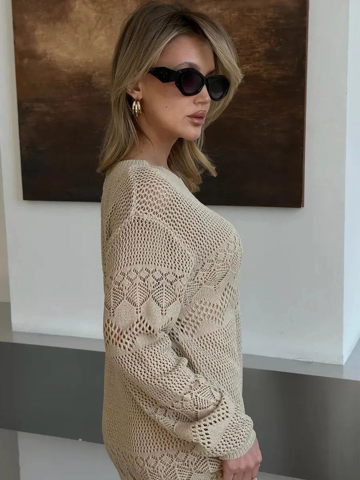 Elegant woman in shades wearing the Verona Maxi Dress by Lauven, showcasing its intricate beige crochet knit design.