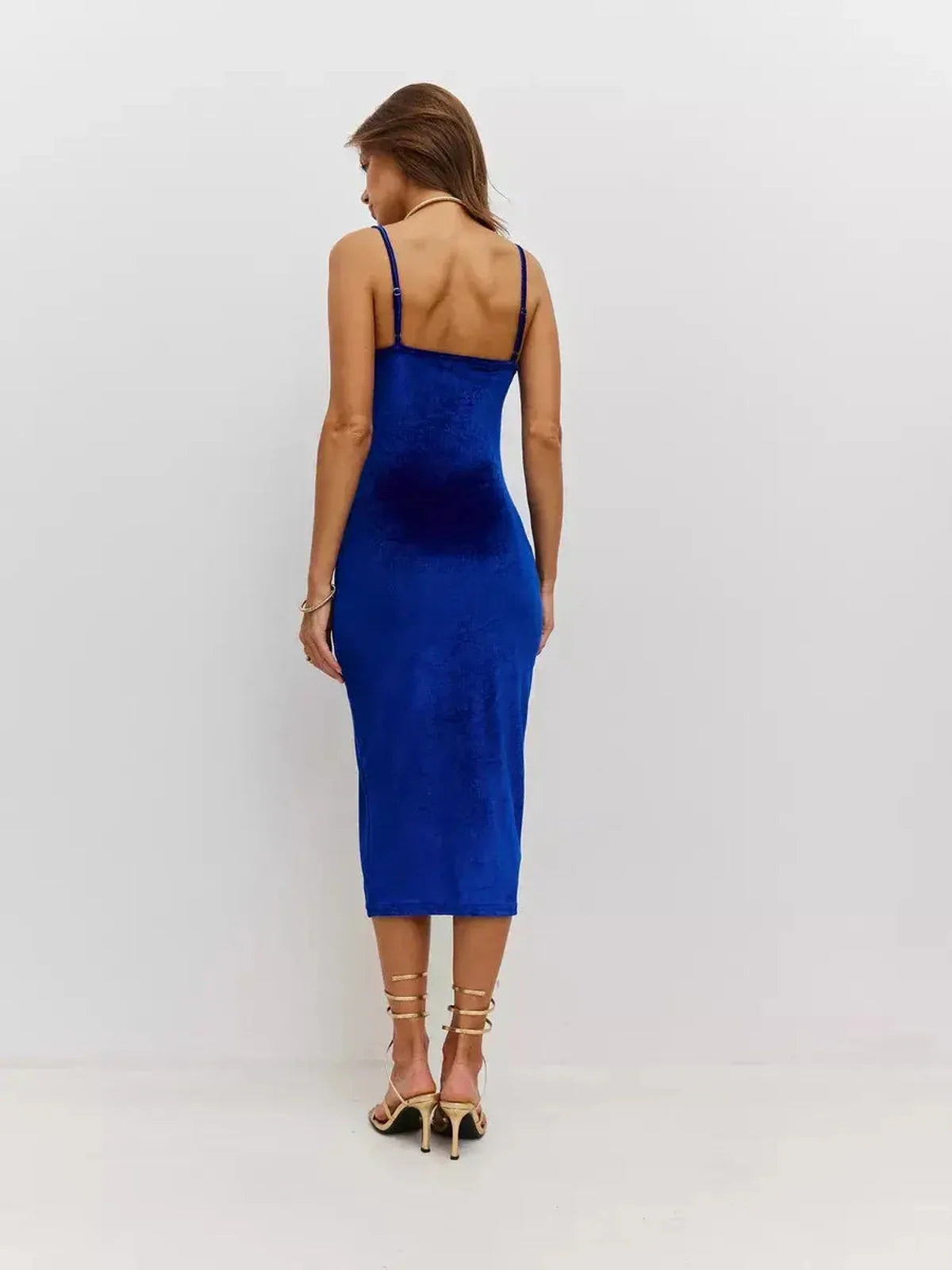 Back view of a woman in a royal blue velvet midi dress with thin straps, showcasing its elegant silhouette.