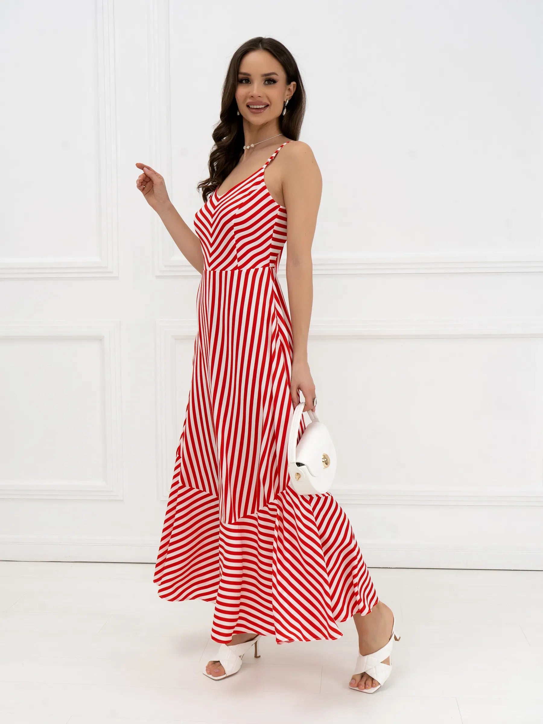 Model wearing a striped red-and-white maxi dress with chevron design and a tiered hem, accessorized with a white bag.