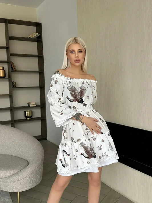 Model in a white crane print mini dress with long sleeves, showcasing summer elegance and modern artistry.