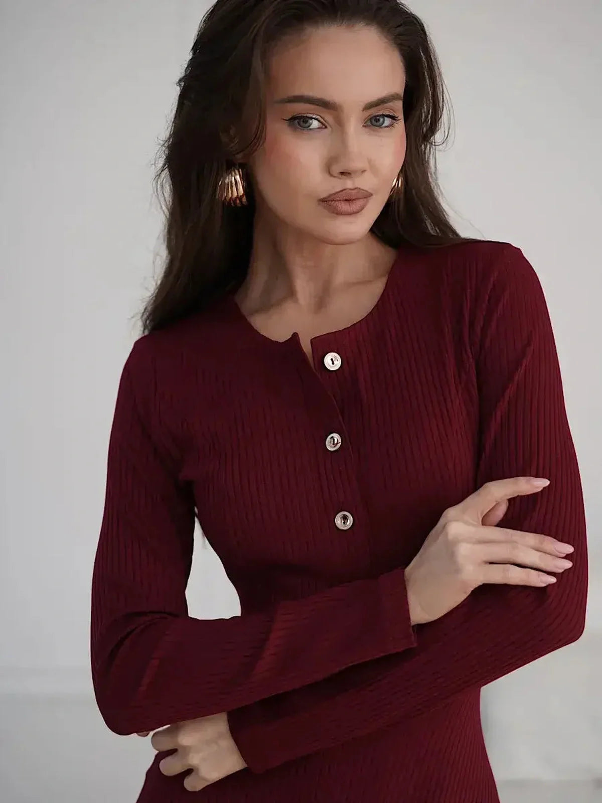 Model wearing a burgundy ribbed midi dress with gold button detail, showcasing elegance and sophistication.