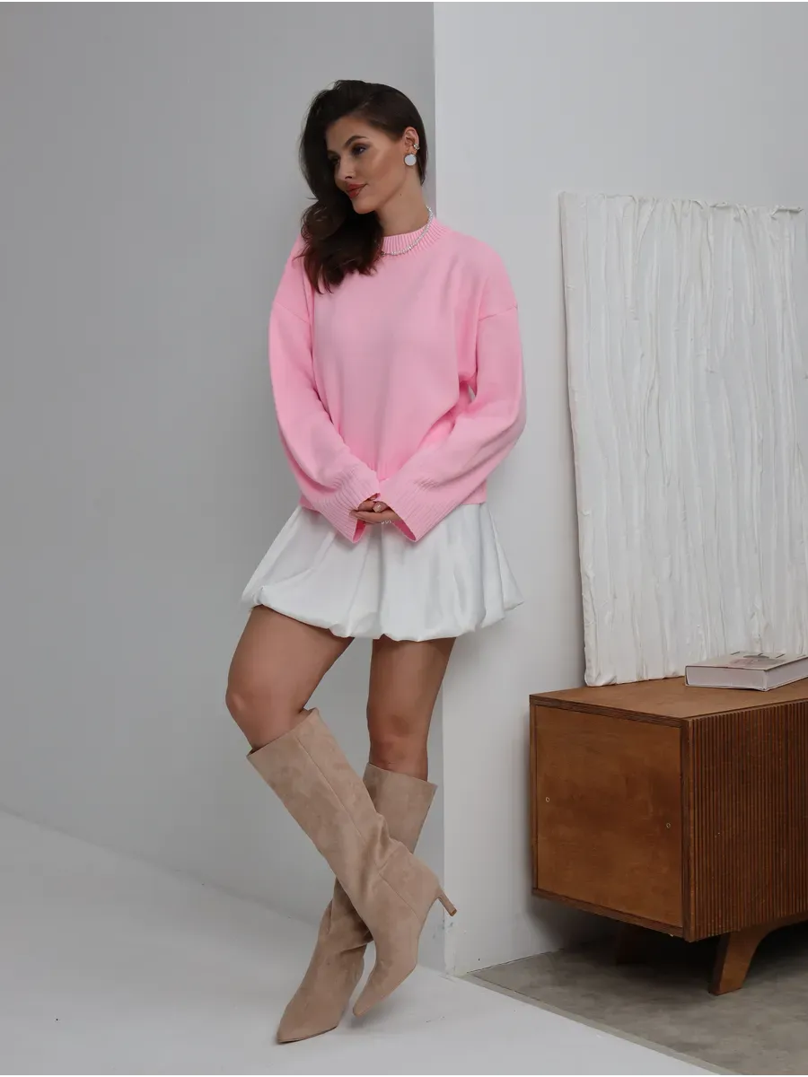 Model showcasing the Lyra Sweater in soft pink by Lauven, paired with a white skirt and knee-high boots.