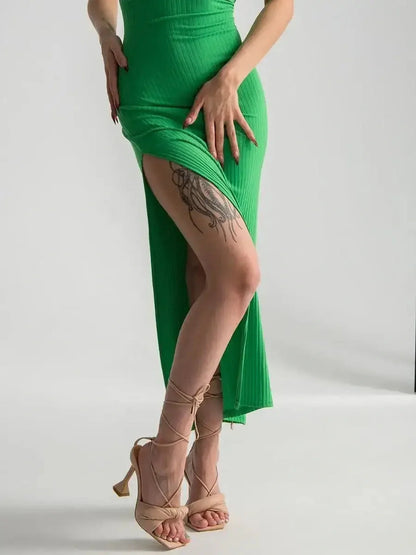 Model showcases the Maxi Dress Emerald Whisper with a bold leg slit and strappy back, epitomizing contemporary elegance.