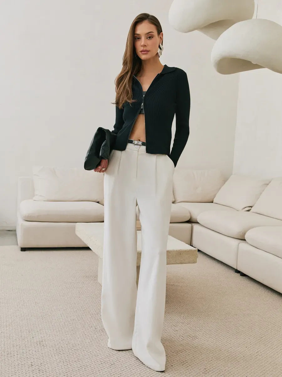 Stylish woman wearing Lauven Nova Cardigan, black ribbed knit with two-way zipper, paired with white wide-leg pants.