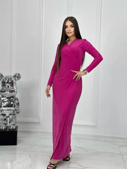Model wearing the elegant Velora Maxi Dress in rich pink with long sleeves and a side slit, showcased in a stylish interior.