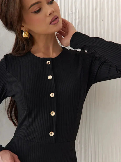Close-up of a woman in a black ribbed midi dress featuring decorative buttons and a chic, elegant neckline.