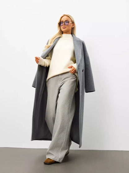 Model showcasing the Liora Sweater, an oversized cashmere knitwear, paired with a long grey coat and wide-leg pants.