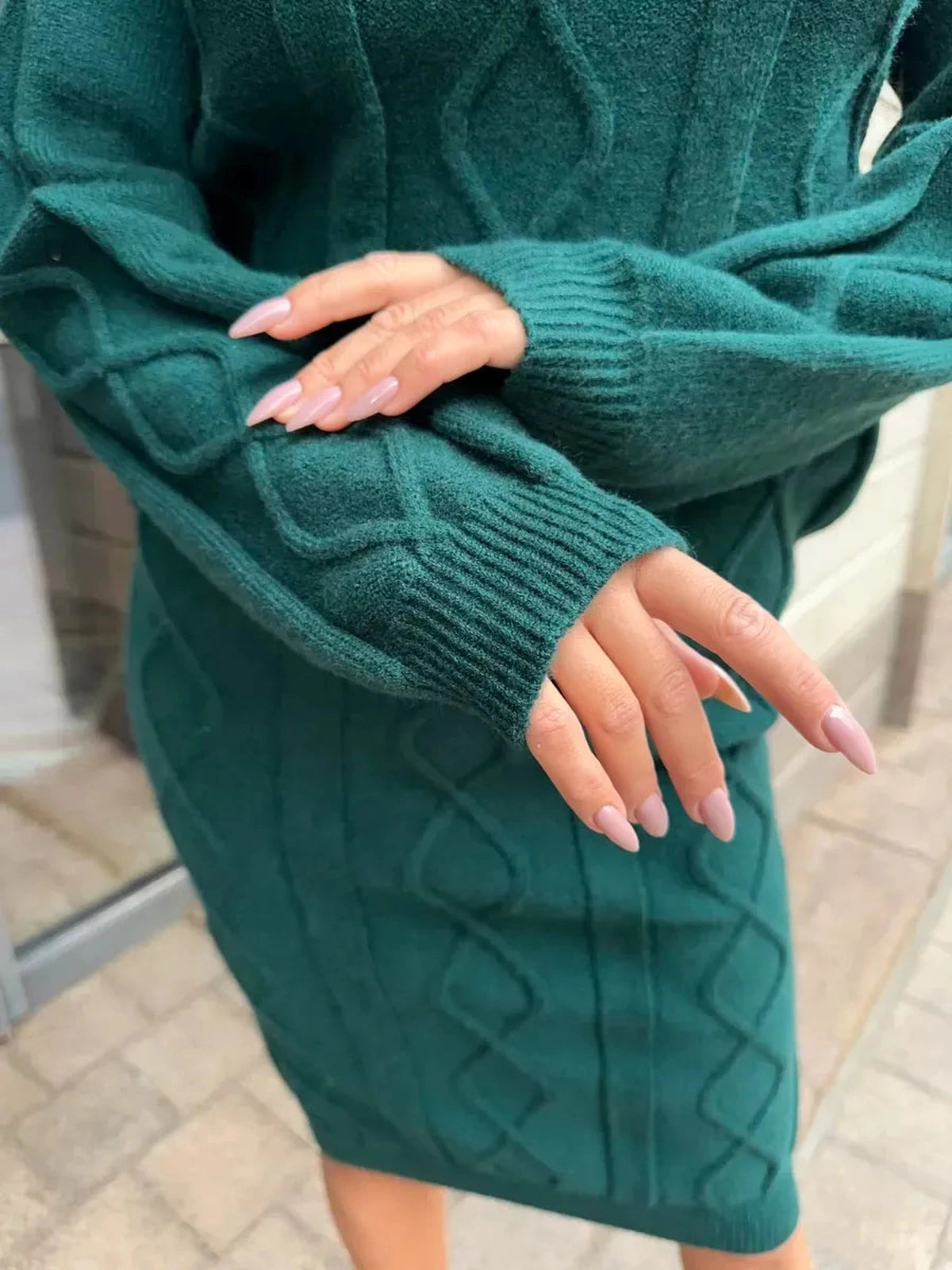 Close-up of hands in Selene Midi Dress by Lauven, showcasing textured knit fabric and the elegant emerald color.