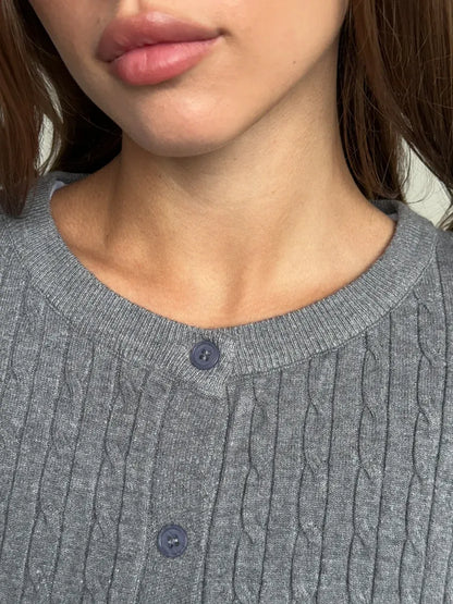 Close-up of a woman wearing the Sterling Cardigan by Lauven, showcasing the grey cable knit detail and button closure.