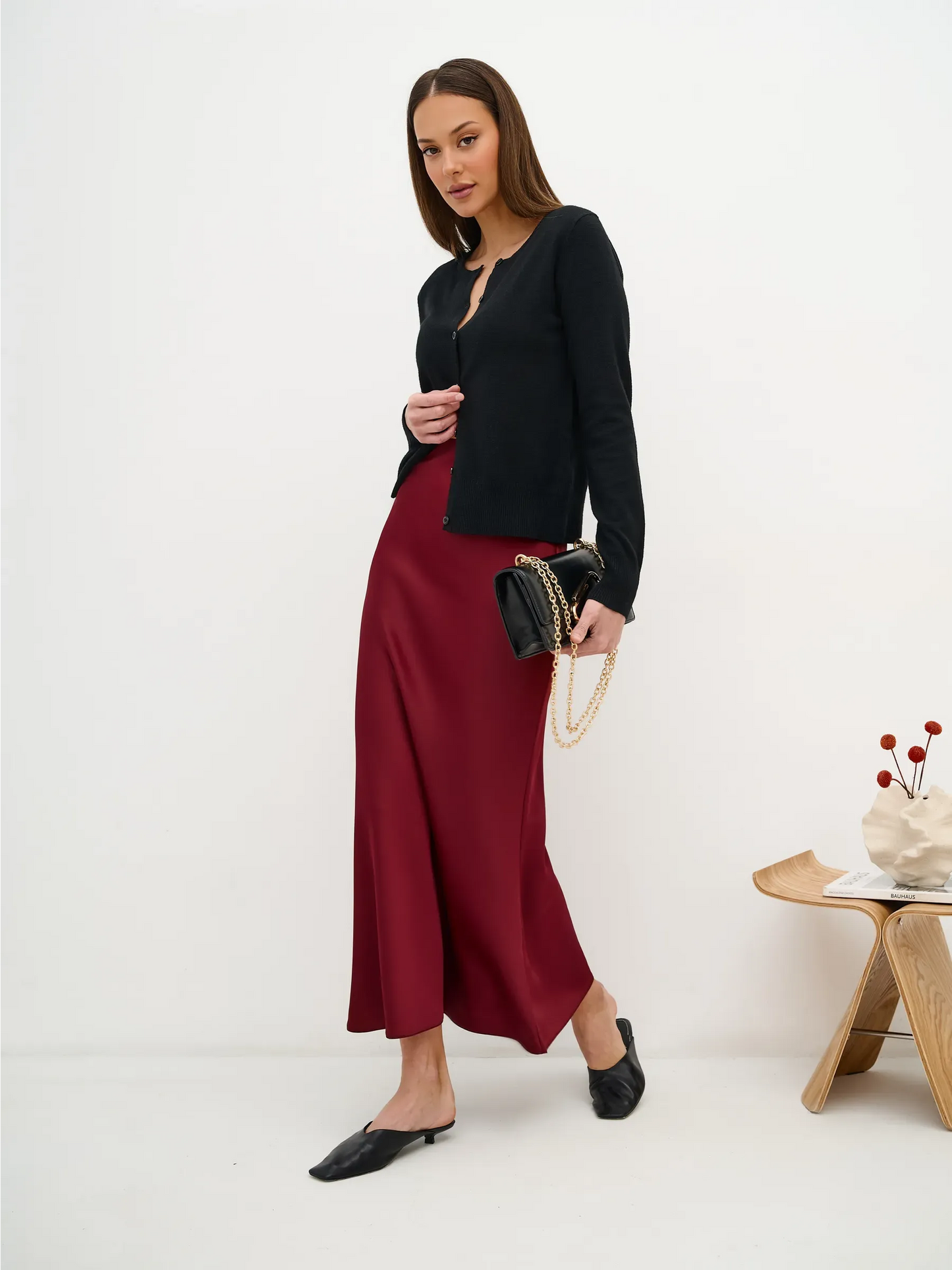 Model wearing Orion Cardigan by Lauven with a burgundy skirt, showcasing sleek black knitwear and stylish accessories.
