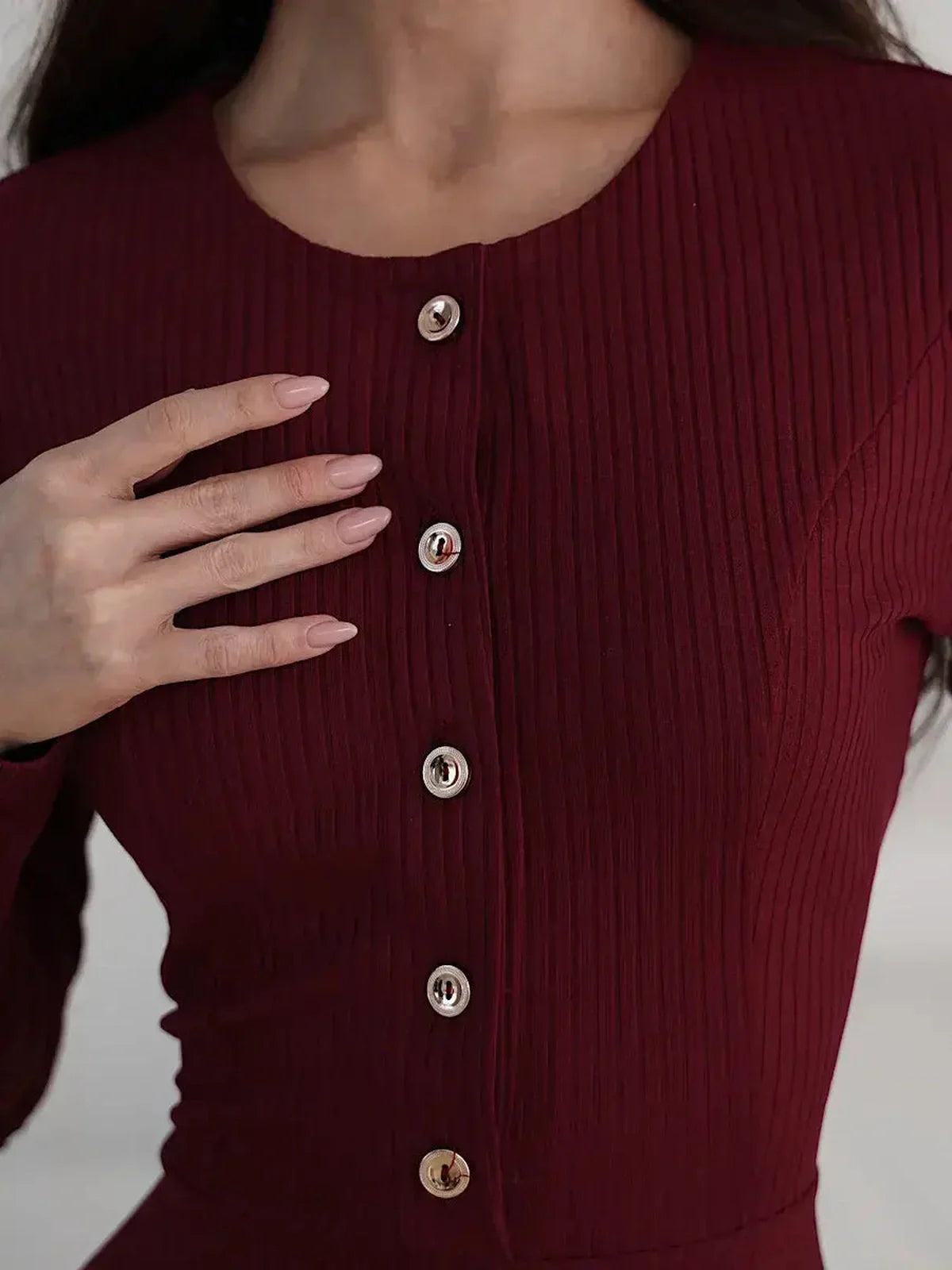 Close-up of ribbed burgundy dress featuring gold-tone button detail and long sleeves.