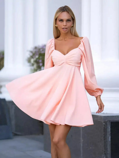 Model wearing a blushing peach mini dress with voluminous sleeves and flattering ruched bodice, ideal for summer.