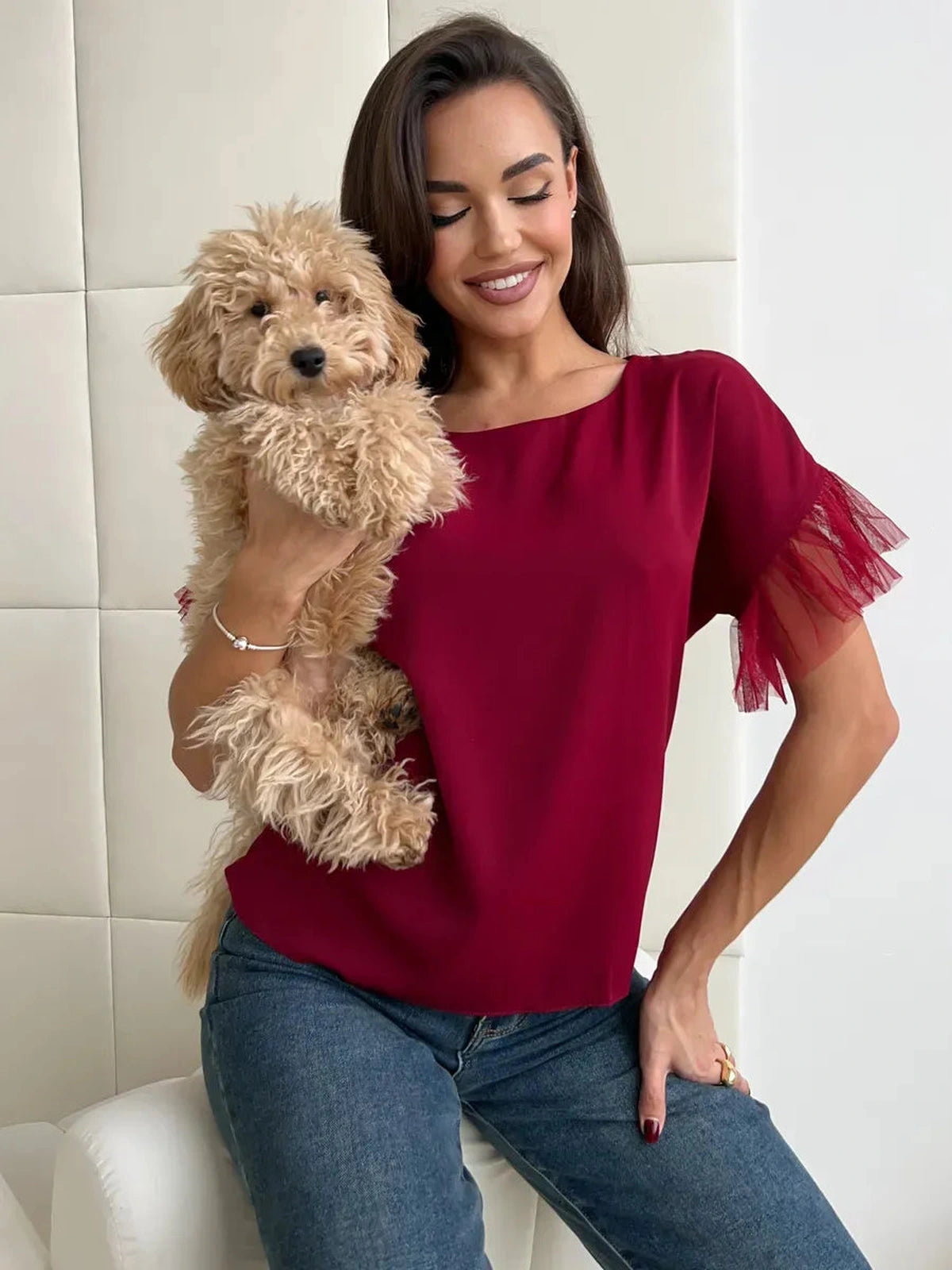 Woman in Velora Blouse by Lauven, burgundy with sheer ruffle sleeves, holding a tan fluffy dog.