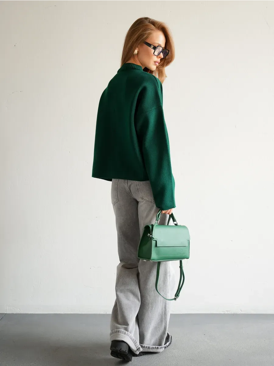 Model wearing a Verdant Cardigan by Lauven, styled with gray jeans and a green handbag.