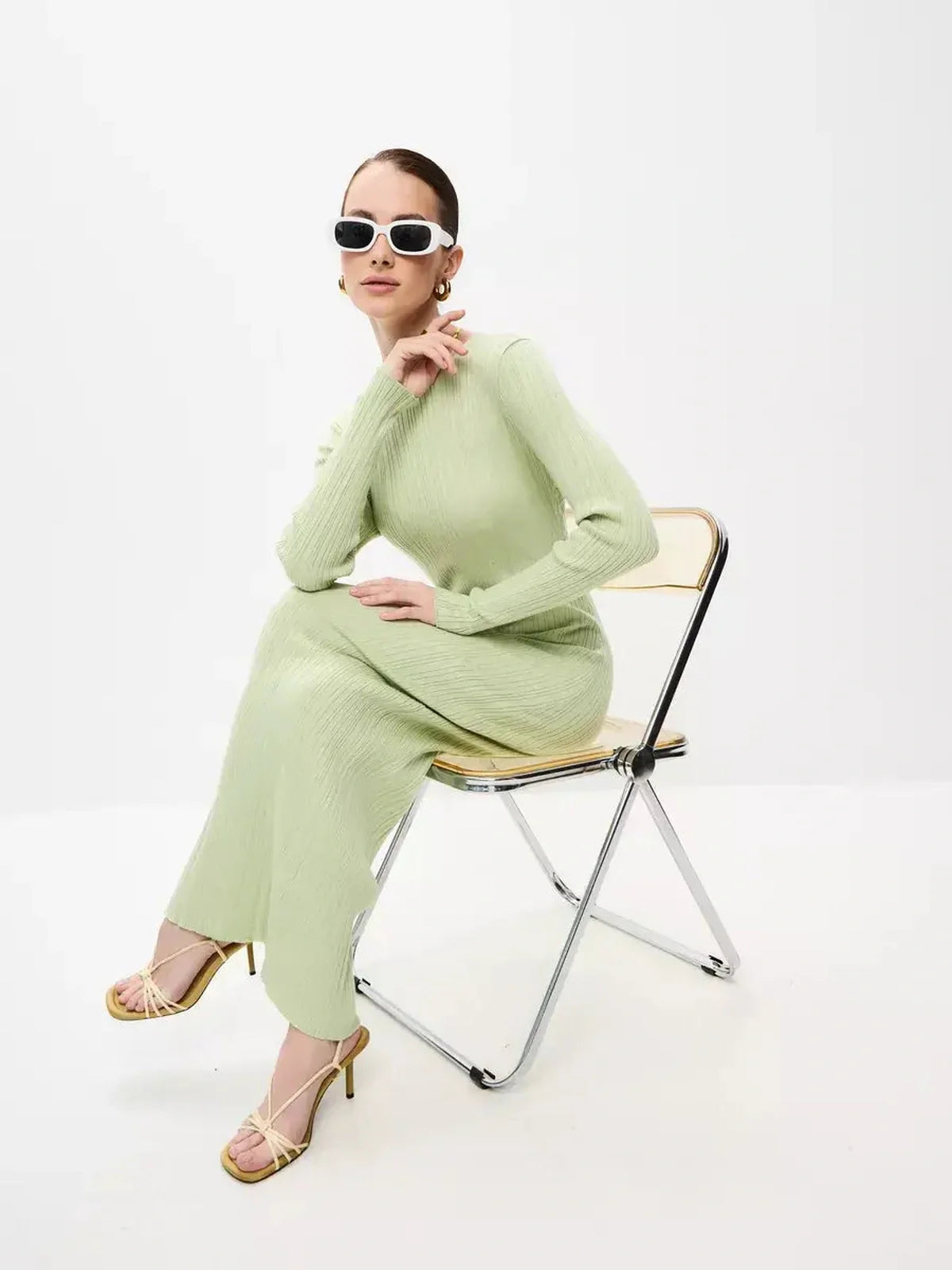 Model wearing Celery Luxe Maxi Dress in light green, showcasing seamless elegance and sculpted fit, seated on a chair.