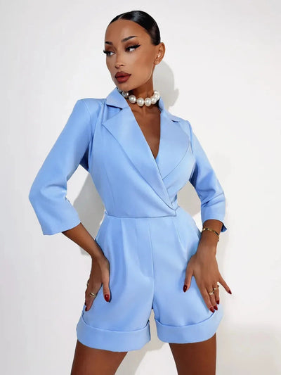 Fashionable woman wearing a chic blue jumpsuit, accessorized with a pearl necklace, posing confidently against a neutral background.